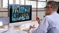 a man sitting at a desk in front of a computer screen with people on it