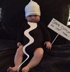 a baby sitting on a bed holding a sign that says same costume as last year