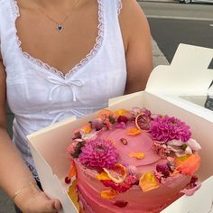 a woman holding a box with a pink cake in it and flowers on the top