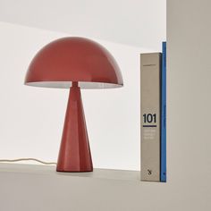 a red lamp sitting on top of a white shelf next to a blue box and a book