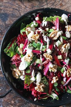 a salad in a black bowl with dressing and nuts on the side, ready to be eaten