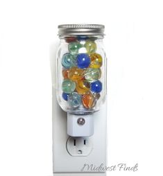 a glass jar filled with colorful marbles on top of a white wall mounted outlet