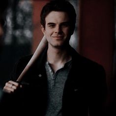 a young man holding a baseball bat in his right hand and smiling at the camera