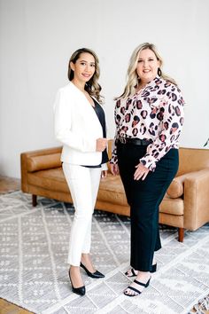 two women standing next to each other in front of a brown couch and white rug