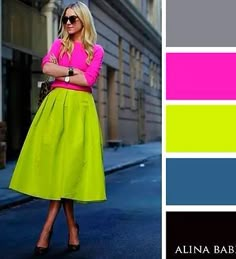 a woman in a pink shirt and green skirt is standing on the street with her arms crossed