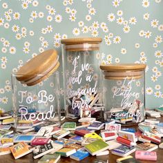 three glass jars with writing on them sitting on a table covered in cards and magnets