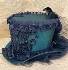 This is elegant Victorian gothic Hand made Bottle green satin Top hat with black back beautifully hand crafted feathers and bows black net bustle train.Top Hat with Black laces and 3D silk flowers and black pearls and jewels and sequences hand stitched. There is brass buckle at the side.Please refer to the photos.This is stunning Victorian Steampunk Handmade top hat made with lots of love.It is very well made, this hat is made of a Black satin type of fabric and the inside of the hat is has a Bl Fitted Fantasy Costume Hats For Themed Events, Vintage Fitted Top Hat For Cosplay, Fitted Steampunk Top Hat For Themed Events, Steampunk Fitted Top Hat For Themed Events, Fitted Gothic Costume Hats And Headpieces For Themed Events, Fitted Gothic Costume Hats For Themed Events, Fitted Vintage Costume Hats And Headpieces For Cosplay, Fitted High Crown Costume Hats And Headpieces, Vintage Fitted Costume Hats And Headpieces For Cosplay