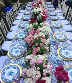 a long table is set with blue and white china plates, pink and red flowers