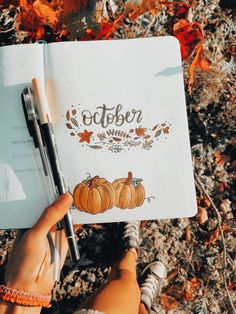 a person holding a notebook with the word october written on it and some pumpkins