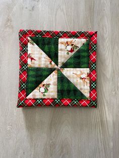 a quilted patchwork square with reindeers and plaid on the bottom, sitting on a wooden surface