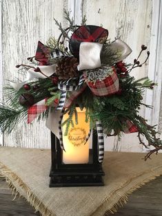 a christmas lantern with pine cones, evergreen and plaid ribbon on it sitting on a burlock