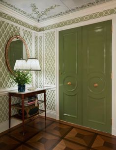 a green door in a room next to a table with a lamp and mirror on it