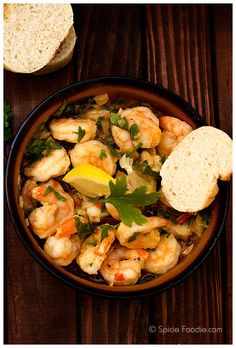 a bowl filled with shrimp and bread on top of a wooden table next to a piece of bread