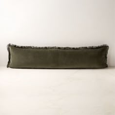 an olive green velvet pillow with frayed edges on a marble surface, against a white wall