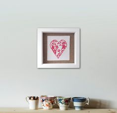 three cups are sitting on a shelf in front of a framed heart