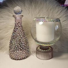 a white candle and a glass vase sitting on a fur covered table top next to each other