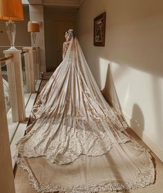 a woman in a wedding dress standing next to a bed with a long veil on it