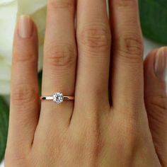 a woman's hand with a diamond ring on her finger and white flowers in the background