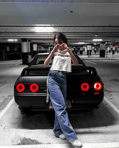 a woman standing next to a black car in a parking lot with her hands on her face