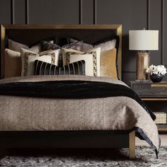 a bed with black and gold pillows on top of it next to a night stand