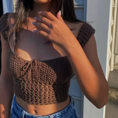 a woman wearing a brown crop top is holding her cell phone up to her chest