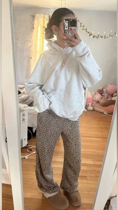 a woman taking a selfie in the mirror wearing leopard print pants and a white sweatshirt