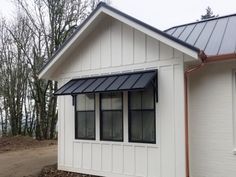 a small white house with a black metal roof and windows on the side of it