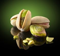 two pistachios and one piece of fruit on a reflective surface with green background