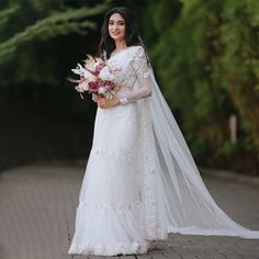 a woman in a white wedding dress holding a bouquet and posing for the camera with her veil over her head