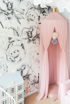 a pink canopy bed sitting next to a wall with flowers on it and a doll house in the corner