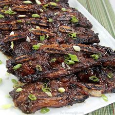 grilled meat with green onions and seasoning on a white platter, ready to be eaten