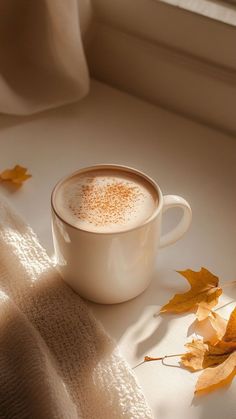 a cappuccino is sitting on a table with autumn leaves