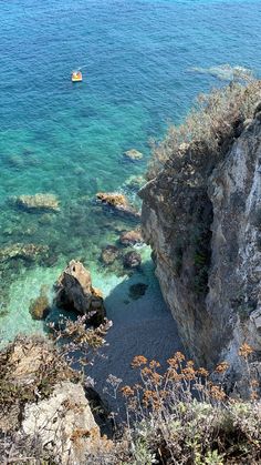 a boat is in the water near some rocks and plants on the shore with clear blue water