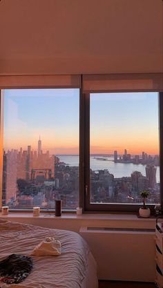 a bedroom with two large windows and a view of the city from it's bed