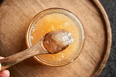 a person holding a wooden spoon over a jar filled with honey and ice cubes