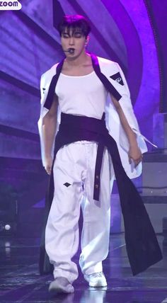 a male in a white shirt and black belted pants is on stage with purple lighting behind him