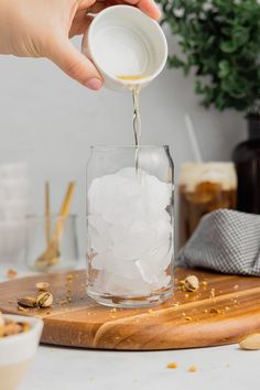 someone pouring sugar into a glass filled with ice and nuts on a wooden cutting board