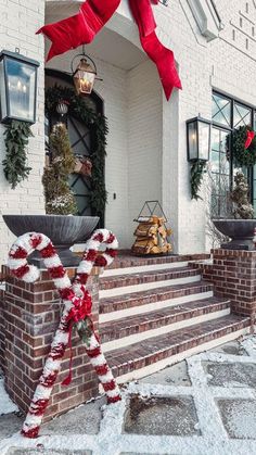 christmas decorations on the front steps of a white brick building with red ribbon and wreaths
