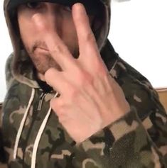 a man in camo jacket making the vulcan sign with his hand while wearing a hat