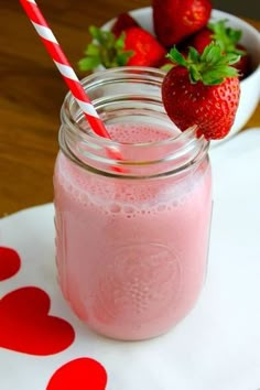 a strawberry smoothie in a mason jar with two strawberries on the table next to it