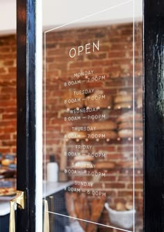 an open sign in front of a brick wall with pastries on the table behind it