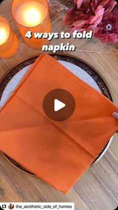 an orange napkin sitting on top of a wooden table next to two candles and flowers