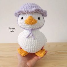 a hand holding a small white crocheted penguin with a purple hat on it's head