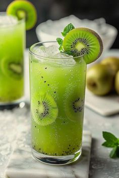 two glasses filled with green liquid and kiwi slices on top of each glass,