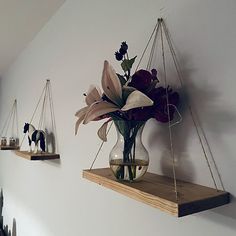 some flowers are in a glass vase on a shelf and hanging from the wall behind them