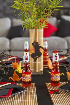 a table topped with bottles of hot sauce next to a vase filled with flowers and leaves