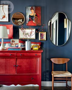 a red dresser with pictures on the wall and a mirror above it, along with a wooden chair