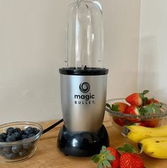 a blender sitting on top of a wooden table next to bowls of berries and bananas