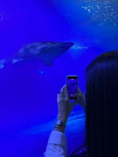 a woman taking a photo of two dolphins in an aquarium with her cell phone while looking at them