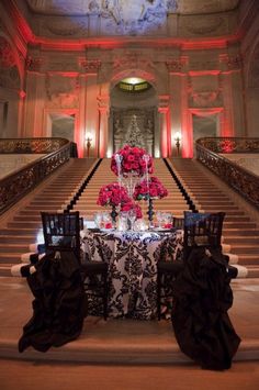 a table with flowers on it sitting in front of some stairs and chandeliers